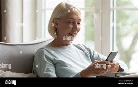 Happy Mature Woman Sitting On Cozy Couch Using Smartphone Stock Photo Alamy