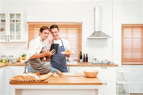 Feliz pareja gay caucásica cocinando juntos en la cocina mientras ven cómo cocinar en una