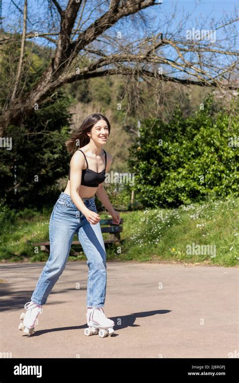 Brunette Woman Skating In The Park Wearing Sports Bra Jeans And Pink Roller Skates Stock Photo
