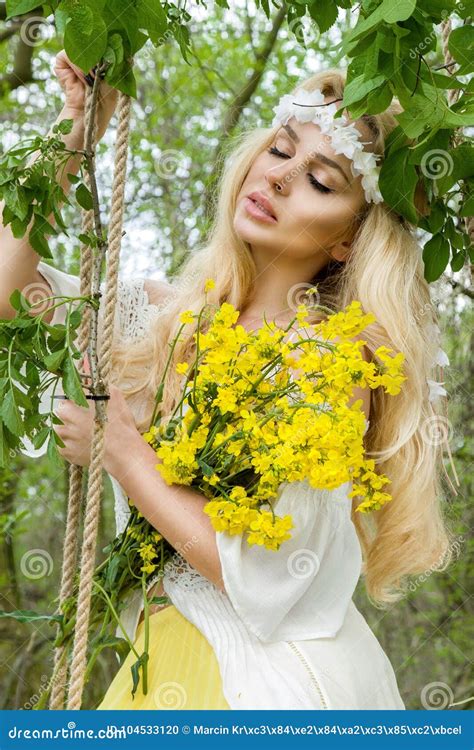 Stunning Blonde Natural Woman Swing On A Swing On A Tree Wearing A Spring Dress Stock Photo