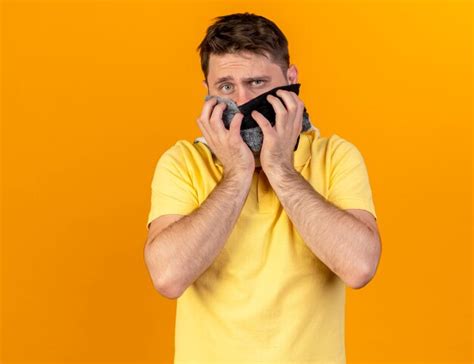 Confus jeune homme slave malade blonde portant et tenant un foulard isolé sur un mur orange avec