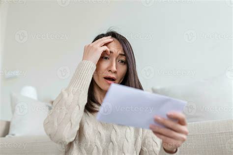 Portrait of a worried Asian woman looking at received letter at home