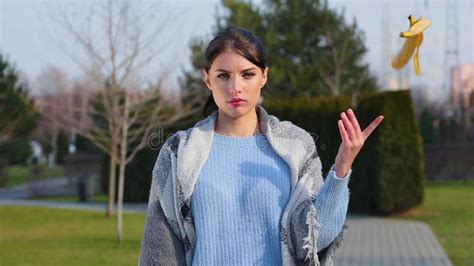 Portrait Attractive Brunette Girl Holds Banana Skin In Her Hand And Throws It On Sidewalk Then