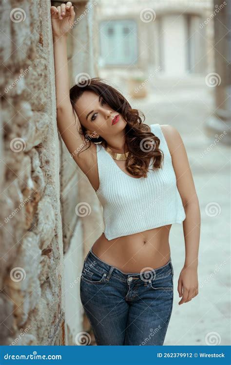 Caucasian Brunette Woman Wearing A White Crop Top And Jeans Leaning On