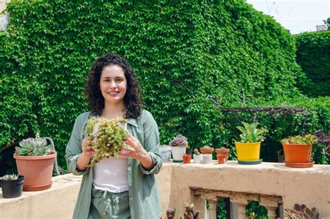Retrato de una joven latina feliz en su jardín sonriendo y sosteniendo una planta en sus manos