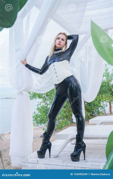 Jeune Fille Blonde Mince D Esclavage Dans La Combinaison Pantalon Noire De Latex Avec Le Corset