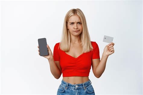 Une fille blonde mécontente grimaces montre un écran de téléphone portable et une moue de carte