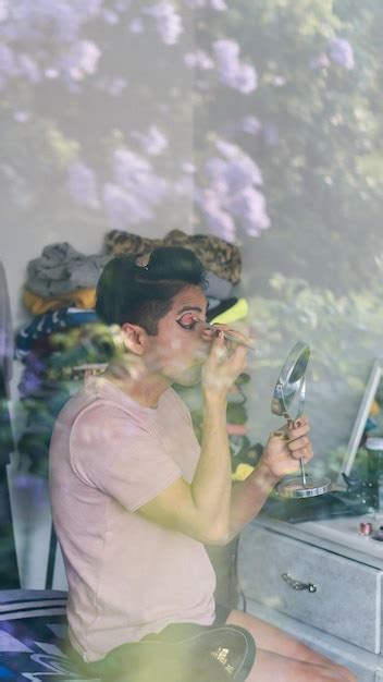 Premium Photo Gay Person Applying Makeup Using A Mirror And Eyeliner Sitting On A Bed