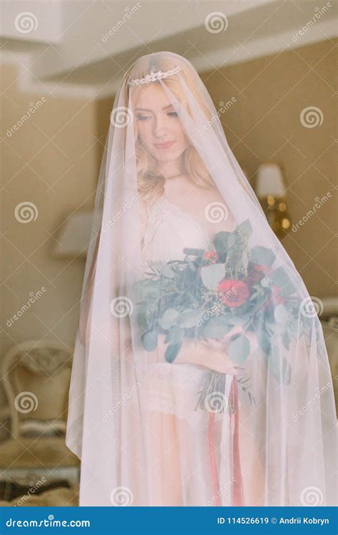 Blonde Bride With Long Veil Dressed In White Underwear Standing On The Bed And Holding Wedding