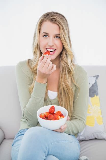 Premium Photo Cheerful Pretty Blonde Eating Strawberries Sitting On Cosy Sofa