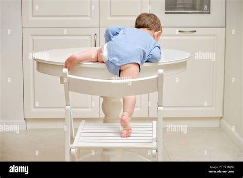 Toddler Baby Climbs On The Kitchen White Table A Child In Danger