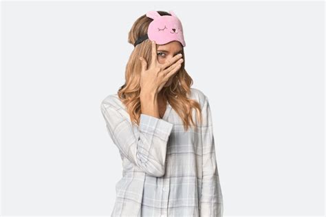 Premium Photo Blonde In Pajamas With Sleep Mask Blink At The Camera Through Fingers