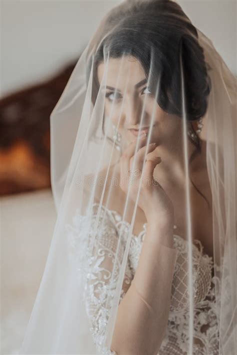 Portrait A Brunette Bride In A White Dress Wrapped In A Veil Looks Down And Touches Stock