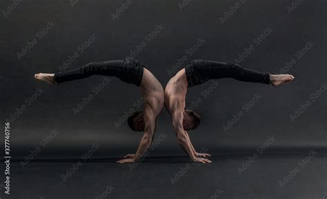 Two Twin Brothers In Black Jeans With A Naked Torso Perform Acrobatic Elements Black Background