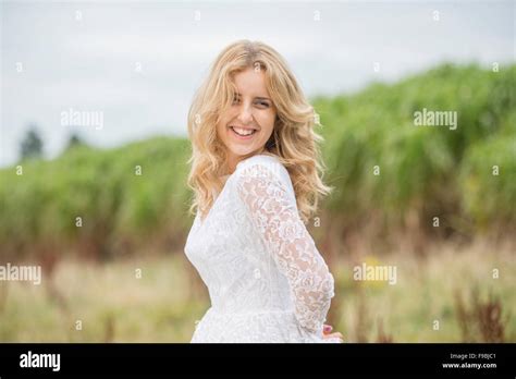 Glückliche Braut Eine junge blonde behaarte Frau trägt ein Spitzen weißes Brautkleid im Freien