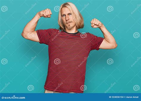 Caucasian Man With Blond Long Hair Wearing Casual Striped T Shirt Showing Arms Muscles Smiling