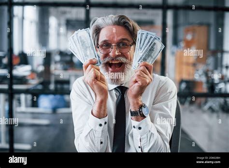 Happy Mature Businessman With Grey Hair And Beard In Formal Clothes Is In The Office Holding