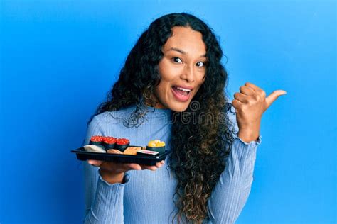 Joven Latina Que Muestra Un Plato De Sushi Apuntando El Pulgar Hacia El Costado Sonriendo Feliz