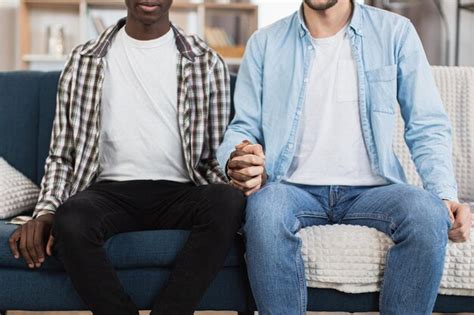 Close up do casal gay multirracial de mãos dadas no sofá Foto Premium