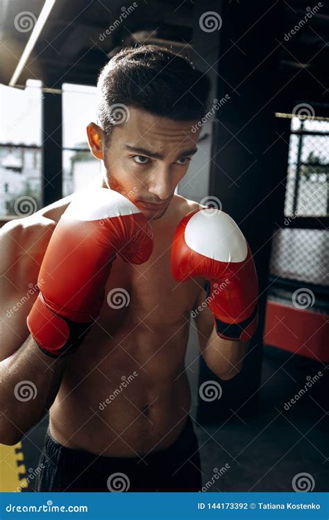 Sportsman With A Naked Torso Keeps His Hands In The Red Boxing Gloves Next To His Face In The