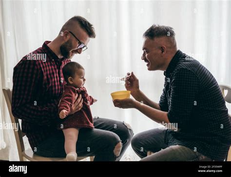Homme gay couple avec adopté bébé fille à la maison Deux beaux pères nourrissent la petite