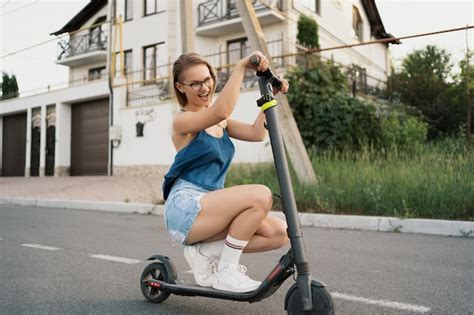 Menina bonita montando uma scooter elétrica no verão na rua Foto Grátis