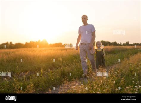 Dad And His Blonde Daughter Are Walking And Having Fun In A Chamomile Field The Concept Of