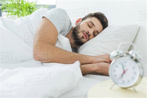 Handsome Bearded Man Sleeping In Bed In The Morning Alarm Clock On