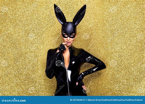 Blonde Woman Posing In Halloween Vinyl Black Costume And Black Bunny Mask On On A Glitter Gold