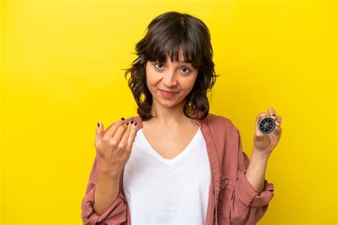 Jovem mulher latina segurando bússola isolada em fundo amarelo convidando para vir a mão