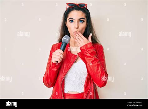 Brunette Teenager Girl Singing Song Using Microphone Covering Mouth With Hand Shocked And