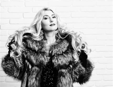 Rich Curly Blonde Woman In Black Leather Pants Top And Wide Brimmed Hat Stands Sideways Looking