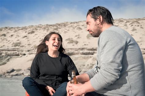 Joven Pareja Latina Sentada En La Playa Hablando Y Bebiendo Foto Premium