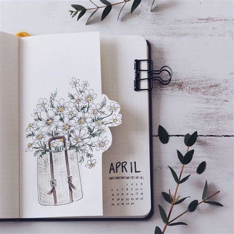 An Open Notebook With Flowers In A Vase On The Cover Next To Some