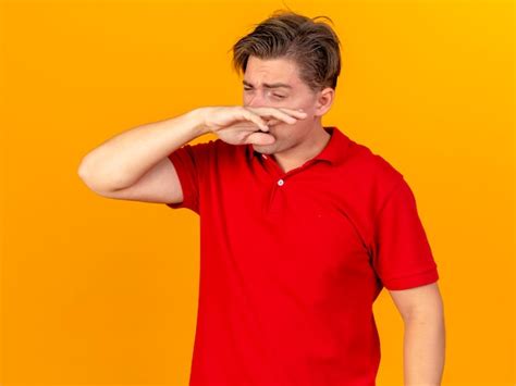 Fronçant les sourcils jeune bel homme malade blonde essuyant son nez avec la main avec les yeux