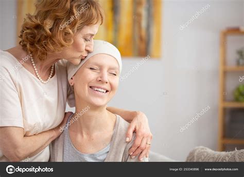 Senior Redhead Woman Kissing Forehead Of Her Happy Lesbian Partner Suffering From Bone Tumor