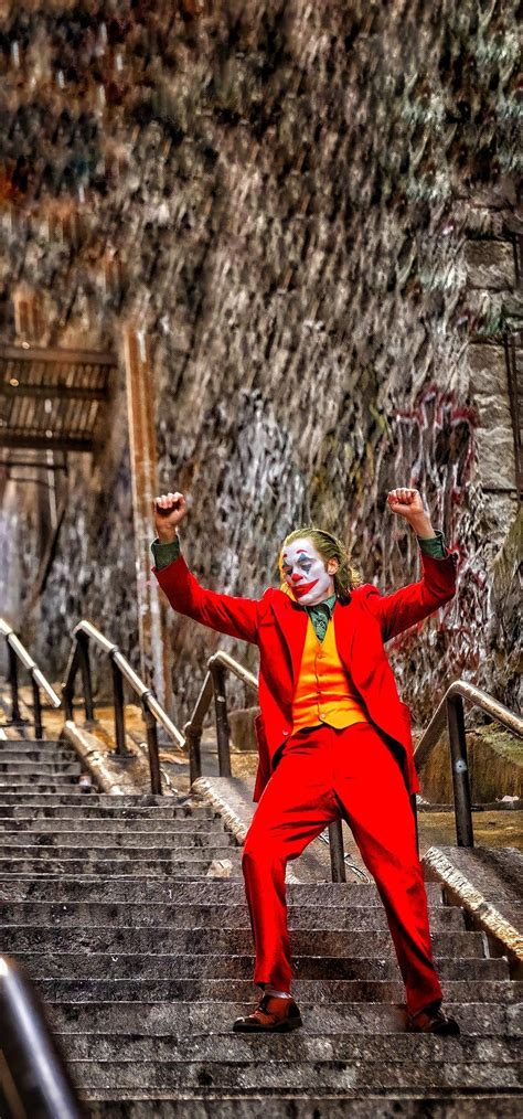 A Man Dressed As The Joker Standing On Some Stairs With His Arms In The Air