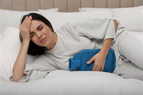 Woman Using Hot Water Bottle To Relieve Menstrual Pain On Bed At Home Stock Photo Image Of
