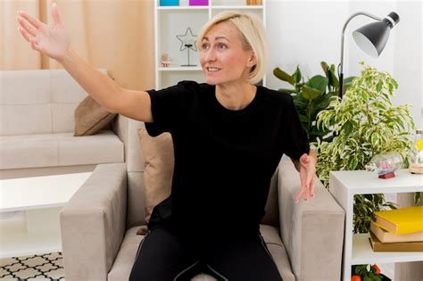 Joyeuse Belle Femme Blonde Est Assise Sur Un Fauteuil Regardant Et Pointant Sur Le Côté Photo