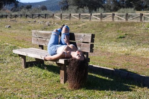 Spanish Brunette Curly Haired Woman Lying On A Bench On The Path Leading To The Forest She Is
