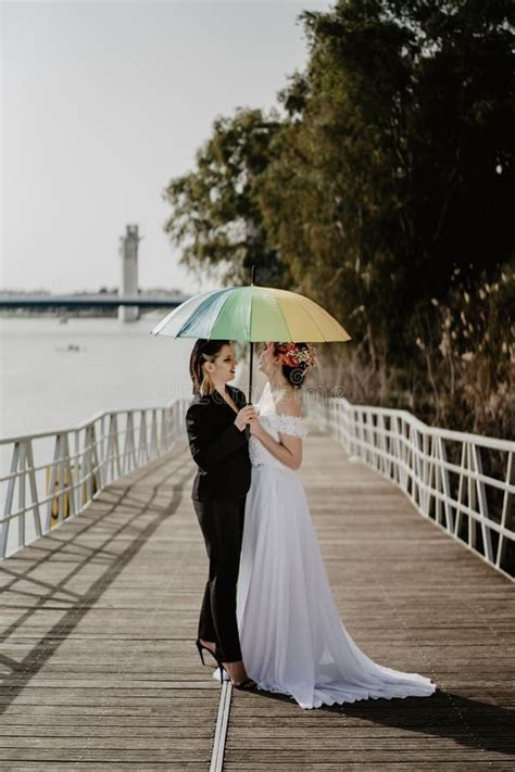 Vertical Closeup Of A Lesbian Pair A Bride And A Female In Black Holding A Rainbow Umbrella