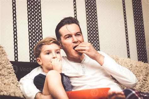 Embraced Father And Son Eating Popcorn And Watching Tv At Home