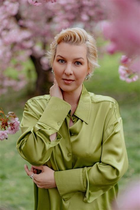A Blonde Woman In Green Outfit Poses Surrounded By Cherry Blossoms Outdoors Stock Photo Image