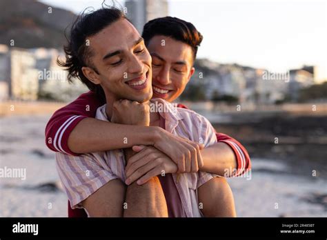 Happy Biracial Gay Male Couple Embracing And Smiling On Beach At Sundown Stock Photo Alamy