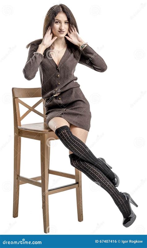 Beautiful Brunette Girl Posing On A Chair In A Long Sweater And Woolen Stockings Stock Photo