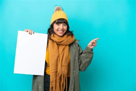Jovem Mulher Latina Vestindo Jaqueta De Inverno Isolada Em Fundo Azul Segurando Um Cartaz Vazio