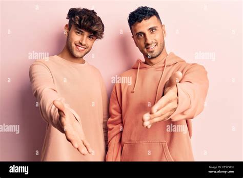 Jeune gay couple portant des vêtements décontractés souriant gai offrant main de paume donnant