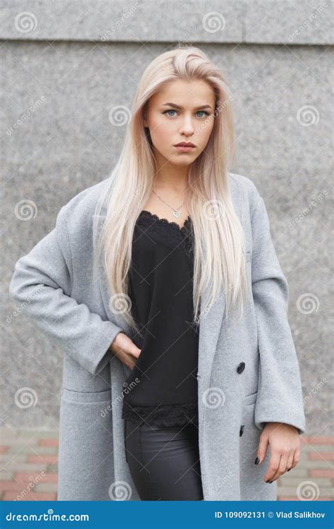 Portrait D Une Belle Jeune Femme Blonde Dans Le Manteau Gris Et Le Pantalon En Cuir Noir Regard