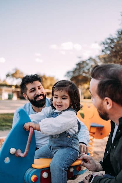 Pareja gay masculina jugando con su hija en un balancín en el parque concepto de familia moderna
