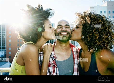 Women Kissing Man S Cheeks On Urban Rooftop Stock Photo Alamy